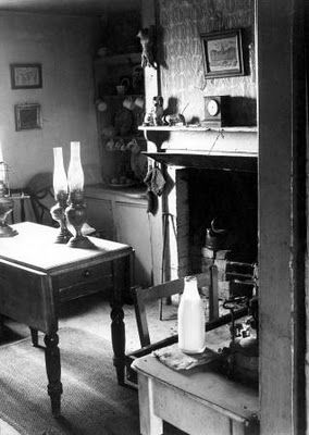 OIl lights in a 1950s rural interior showing fireplace and Victorian furniture.