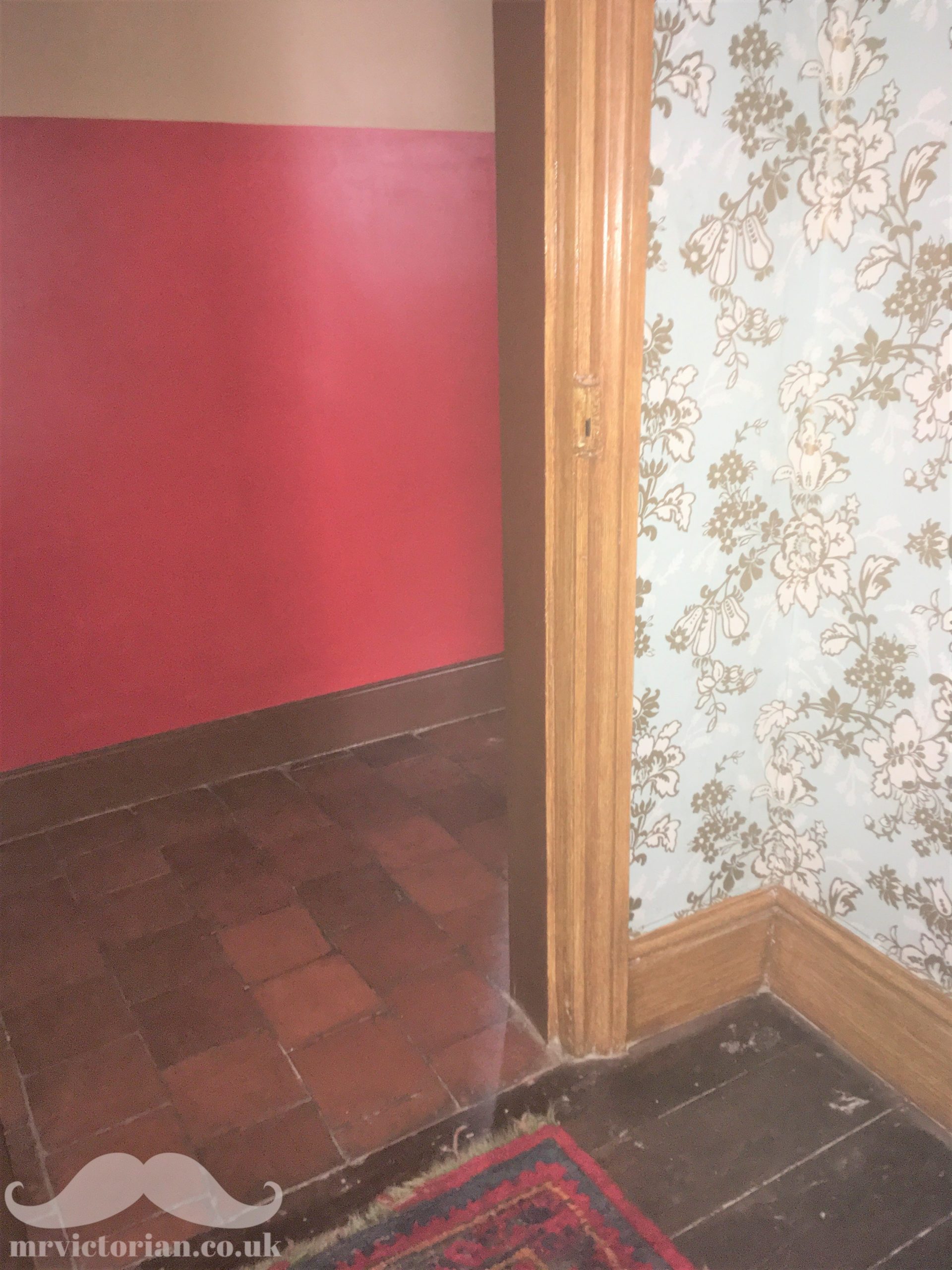 Photograph showing a doorway with a parlour with woodgrained woodwork and floral wallpaper against a plainer inner hallway with painted walls and brown woodwork.