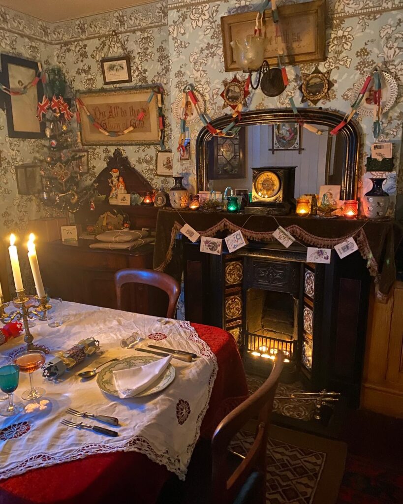 Victorian parlour at Christmas showing lit candelabra, fairy lamps and gas light over the fireplace. 