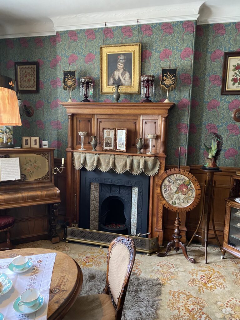 Parlour in typical Victorian interior style with lots of ornaments and knick-knacks on the mantlepiece and piano.