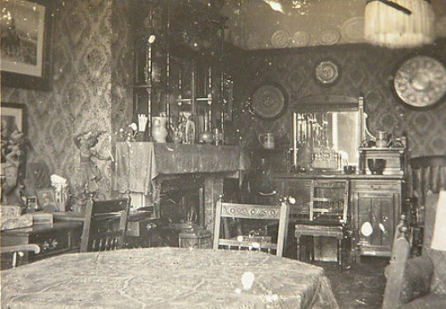 1900s photograph of a dining room or parlour with floral wallpaper.